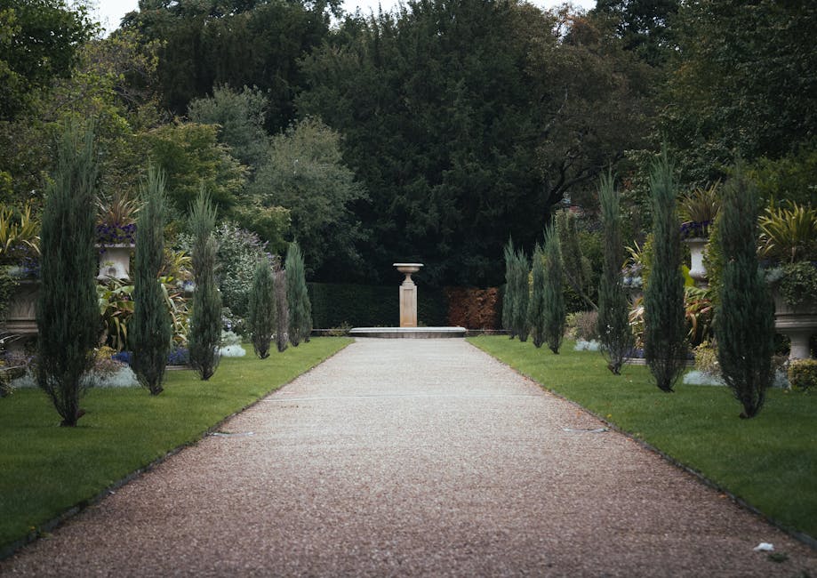 The image depicts a well-maintained garden in front of a traditional red brick house with white-framed windows and a sloped tiled roof. The garden features neatly trimmed hedges bordering a lush green